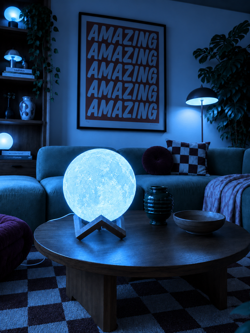 Yuvarlak ahşap masada mavi ışıkla yanan Luna Prism lambası.